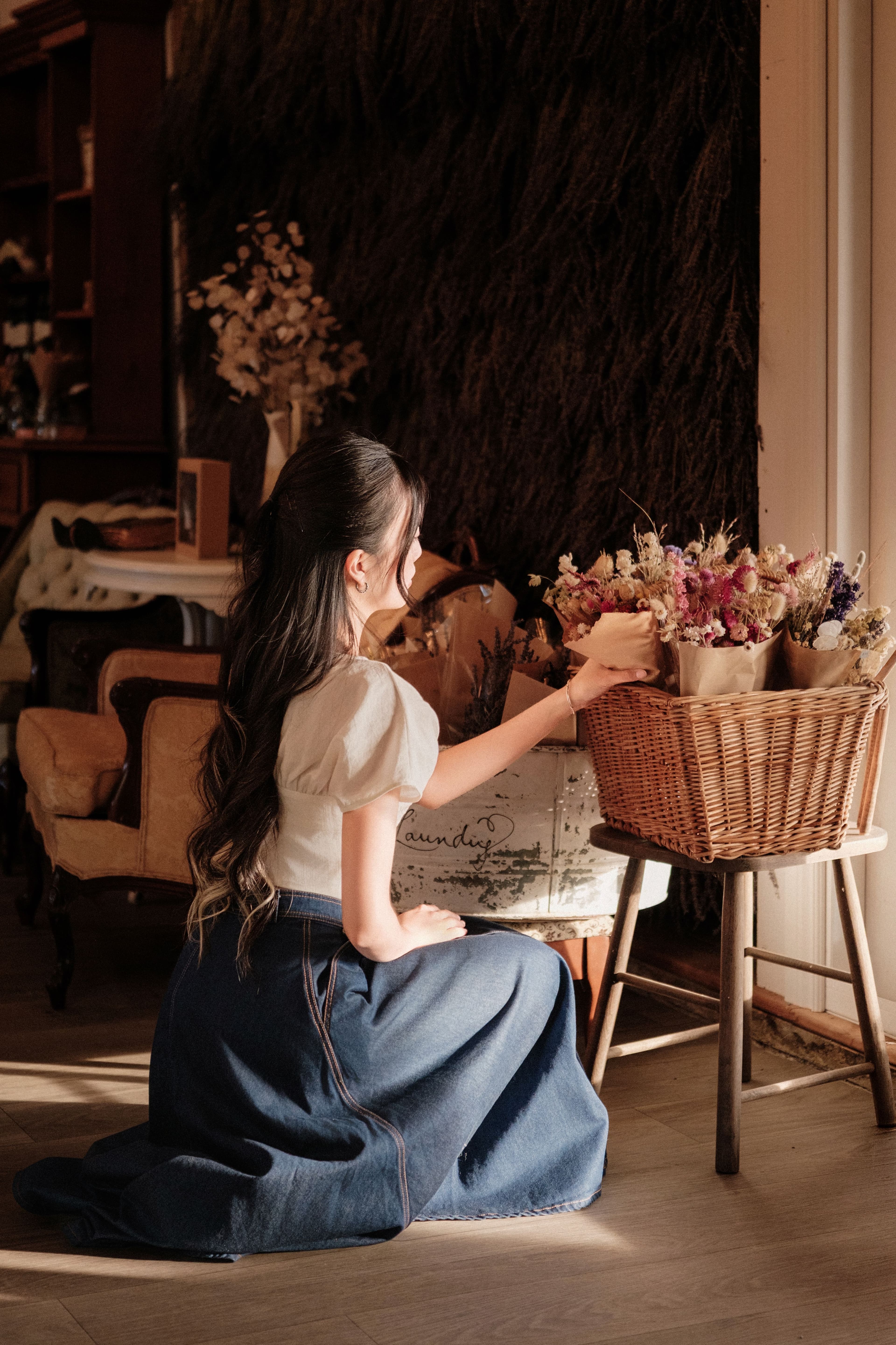 Close portrait of a woman surrounded by hanging dried flowers in warm light.